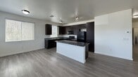 This 1,290 square foot single-story apartment offers a well-designed layout with 2 bedrooms, 2 bathrooms, and a combined kitchen and living area. The kitchen is a standout feature, equipped with dark espresso cabinetry, granite countertops, black appliances including a gas range, microwave, and refrigerator, and a central island that provides additional prep space. Track lighting overhead and wood-look flooring throughout the main areas enhance the modern aesthetic. The open-concept design connects the kitchen seamlessly to the living room, which features a ceiling fan, a sliding glass door leading to an outdoor area, and a window that allows natural light to fill the space. Both bedrooms are carpeted and include ceiling fans and windows with blinds. The primary bedroom measures 150 square feet and connects to a bathroom with a tub/shower combo and an adjacent walk-in closet with wire shelving. The second bathroom mirrors the first in style, featuring a dark vanity with a marble-style countertop, a large mirror, and a tub/shower combo with white tile surround. A dedicated laundry room houses a full-size washer and dryer with overhead wire shelving, completing this functional and contemporary unit.