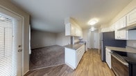 This single-floor unit offers a practical and well-organized layout connecting the kitchen and living areas in an open, flowing arrangement. The kitchen is a standout feature, configured as a galley-style space with ample white cabinetry — both upper and lower — paired with gray laminate countertops. Stainless steel appliances include a refrigerator and electric range, complemented by a built-in dishwasher and a single-basin sink. Wood-look vinyl flooring runs throughout the kitchen and hallway, lending a clean, cohesive feel.

The living area transitions naturally from the kitchen via a peninsula counter, and is finished with neutral-toned carpet that extends into the bedrooms. A ceiling fan with a light fixture adds functionality to one of the bedrooms, which also benefits from a window bringing in natural light. Closet space is well-represented, with at least one bedroom featuring mirrored sliding-door closets with built-in shelving and hanging rods.

The bathroom is finished in a clean, white palette with wood-look flooring, a vanity featuring gray countertops and white cabinetry, and a full-size soaking tub with an overhead shower. The overall design is neutral and move-in ready.