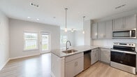This well-appointed single-story home in Port Saint Lucie, Florida, offers three bedrooms and two bathrooms within a thoughtfully designed open-concept layout. The kitchen serves as the heart of the home, featuring gray shaker-style cabinetry, granite countertops, a peninsula island with an undermount sink, stainless steel appliances including a refrigerator, dishwasher, and range, white subway tile backsplash, and pendant lighting overhead. The kitchen flows seamlessly into the living area, which is brightened by multiple windows offering picturesque water views and is equipped with a ceiling fan. Light wood-tone flooring runs throughout the entire home, creating a cohesive and clean aesthetic. The spacious primary bedroom includes windows with serene outdoor views and a ceiling fan. The primary bathroom is finished with a dual-sink granite vanity, wood-tone cabinetry, and a shower-tub combination. The second bathroom mirrors this quality with a tiled tub-shower surround and brushed nickel fixtures. The additional bedrooms are well-sized, each featuring natural light from multiple windows. Neutral paint tones and clean finishes throughout give this home a bright, modern feel suited to Florida living.