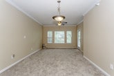 This single-floor residence offers a practical and well-organized layout across several distinct living areas. The kitchen is equipped with ample white cabinetry featuring wood-tone trim, laminate countertops, a double-basin sink, a dishwasher, and an electric range. Hardwood-style flooring runs through the kitchen and bathroom, lending a clean, cohesive look to these functional spaces.

The living areas are generously sized, featuring plush carpet, warm neutral wall tones, and crown molding details. Ceiling fans with integrated lighting are present in the main living spaces, promoting air circulation and comfort. Multiple windows fitted with blinds allow natural light to filter throughout, creating a bright and inviting atmosphere. A glass-paneled exterior door provides convenient access to the outside.

The bedrooms are carpeted and well-proportioned, with one featuring a walk-in closet complete with built-in shelving and a direct connection to the bathroom. The bathroom includes a full tub-shower combination with chrome fixtures and hardwood-style flooring.

A dedicated laundry area accommodates a full-size top-loading washer and dryer side by side, with wire shelving overhead for added storage. Overall, the space maintains a consistent, understated aesthetic with warm neutral tones throughout.