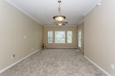 This single-floor residence offers a practical and well-organized layout across several distinct living areas. The kitchen is equipped with ample white cabinetry featuring wood-tone trim, laminate countertops, a double-basin sink, a dishwasher, and an electric range. Hardwood-style flooring runs through the kitchen and bathroom, lending a clean, cohesive look to these functional spaces.

The living areas are generously sized, featuring plush carpet, warm neutral wall tones, and crown molding details. Ceiling fans with integrated lighting are present in the main living spaces, promoting air circulation and comfort. Multiple windows fitted with blinds allow natural light to filter throughout, creating a bright and inviting atmosphere. A glass-paneled exterior door provides convenient access to the outside.

The bedrooms are carpeted and well-proportioned, with one featuring a walk-in closet complete with built-in shelving and a direct connection to the bathroom. The bathroom includes a full tub-shower combination with chrome fixtures and hardwood-style flooring.

A dedicated laundry area accommodates a full-size top-loading washer and dryer side by side, with wire shelving overhead for added storage. Overall, the space maintains a consistent, understated aesthetic with warm neutral tones throughout.