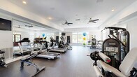 Located at 10840 State Bridge Rd in Alpharetta, GA, this single-floor fitness center offers a comprehensive workout environment designed for both cardio and strength training. The space is bright and open, with large multi-pane windows along multiple walls that bring in abundant natural light and offer views of the surrounding greenery outdoors.

The main workout area is generously proportioned, featuring durable rubber flooring throughout. A row of treadmills, elliptical trainers, and a recumbent stationary bike provide a full suite of cardiovascular equipment. Floor-to-ceiling mirrors are installed along one wall, enhancing the sense of space and allowing users to monitor their form during exercise. Ceiling fans are mounted throughout, ensuring comfortable air circulation during workouts.

A dedicated strength training zone houses a cable machine, an Instinct-brand functional trainer, a weight bench, and a dumbbell rack, catering to a wide range of resistance exercises. A storage rack displays an assortment of stability and medicine balls, while exercise mats are available for stretching and floor work. Wall-mounted flat-screen televisions add an entertainment option for cardio sessions. The clean, neutral color palette with white walls and crown molding trim gives the facility a polished, well-maintained ambiance throughout.