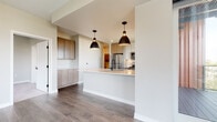 This single-floor residence showcases a cohesive modern design throughout, combining clean lines, neutral tones, and quality finishes. The open-concept kitchen serves as a central highlight, featuring a white-topped peninsula with an integrated sink, warm-toned flat-front cabinetry, stainless steel appliances including a full-size refrigerator and gas range, and a tiled backsplash. Two matte black dome pendant lights hang above the peninsula, adding a contemporary contrast to the light palette. Wood-look flooring in a medium gray-brown tone runs through the main living areas, lending warmth and continuity.

The living areas offer generous proportions with neutral walls and flush ceiling details. A bedroom benefits from an elevated outlook, with large windows on two walls framing urban cityscape views and flooding the space with natural light. A tray ceiling adds architectural dimension to the room.

Two bathrooms reflect the same modern sensibility, each equipped with gray flat-front vanity cabinetry, white countertops, framed mirrors, and matte black fixtures. One bathroom features wood-look flooring and wall-mounted cabinetry for additional storage, while the second includes large-format tile flooring and a separate toilet room. Built-in cabinetry in additional areas provides practical storage throughout the residence.