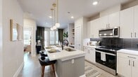 This thoughtfully designed 1-bedroom, 1-bathroom residence offers a cohesive open-concept layout that maximizes every square foot. The kitchen serves as the heart of the home, showcasing crisp white cabinetry, a bold dark subway tile backsplash, stainless steel appliances, and a central island with a quartz countertop and built-in sink. Globe pendant lights suspended from brass fixtures add a warm, modern touch, while bar seating at the island creates an inviting space for casual dining. Light wood-style flooring flows throughout, lending continuity across the living areas. The living room benefits from large windows with horizontal blinds and floor-length drapes, allowing abundant natural light and outdoor views. The bedroom is a comfortable retreat featuring a ceiling fan, generous windows, and light-toned walls that create a calm atmosphere. The bathroom is elongated and functional, offering a white vanity with a quartz surface, black hardware accents, and wood-look flooring. A dedicated walk-in closet adjacent to the bathroom provides practical storage. Overall, the residence presents a clean, contemporary aesthetic with consistent finishes and a bright, airy ambiance throughout.