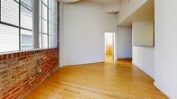 This 650 square foot loft-style apartment in Richmond, VA, combines industrial charm with modern comfort. The space is characterized by its open floor plan, high ceilings, and an abundance of natural light streaming through expansive windows. Exposed brick walls add character and warmth to the interior, contrasting beautifully with the polished hardwood floors throughout.

The apartment features two bedrooms, including a primary bedroom of 130 square feet, offering ample space for rest and relaxation. The single bathroom is efficiently designed with clean lines, featuring a vanity, toilet, and a full-sized bathtub with shower. White tiles and fixtures create a bright, airy feel.

The living areas are spacious and versatile, with the potential for various furniture arrangements. The kitchen, while not visible in the images, is likely integrated into the open plan design. Large windows not only flood the space with light but also offer views of the surrounding urban landscape.

Wood-grain doors and white walls contribute to the apartment's contemporary aesthetic, while exposed structural elements like beams and ductwork maintain the loft's industrial heritage. This apartment successfully balances historic architectural elements with modern living requirements, creating a unique and inviting urban dwelling.