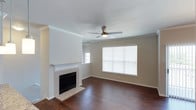 Located in Frisco, this single-story home offers a clean, well-maintained layout designed for comfortable everyday living. The living room serves as the centerpiece of the home, showcasing rich, dark hardwood flooring that extends throughout the space and creates a warm, grounded aesthetic. A classic tile-surround fireplace with a crisp white mantel anchors one wall, providing both a functional heating element and a stylish focal point for the room. Crown molding trims the walls, adding a refined architectural detail that elevates the overall finish of the interior. Natural light pours in through multiple windows fitted with horizontal blinds, illuminating the neutral-toned walls and giving the space an open, airy feel. A ceiling fan with an integrated light fixture is centrally positioned overhead, ensuring year-round comfort and efficient air circulation. The understated color palette of warm beige walls paired with white trim creates a versatile backdrop well-suited to a variety of décor styles. The overall ambiance of the home is clean, bright, and move-in ready, offering a solid foundation for personalization while maintaining a timeless and inviting character throughout.