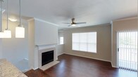 Located in Frisco, this single-story home offers a clean, well-maintained layout designed for comfortable everyday living. The living room serves as the centerpiece of the home, showcasing rich, dark hardwood flooring that extends throughout the space and creates a warm, grounded aesthetic. A classic tile-surround fireplace with a crisp white mantel anchors one wall, providing both a functional heating element and a stylish focal point for the room. Crown molding trims the walls, adding a refined architectural detail that elevates the overall finish of the interior. Natural light pours in through multiple windows fitted with horizontal blinds, illuminating the neutral-toned walls and giving the space an open, airy feel. A ceiling fan with an integrated light fixture is centrally positioned overhead, ensuring year-round comfort and efficient air circulation. The understated color palette of warm beige walls paired with white trim creates a versatile backdrop well-suited to a variety of décor styles. The overall ambiance of the home is clean, bright, and move-in ready, offering a solid foundation for personalization while maintaining a timeless and inviting character throughout.