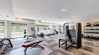 Located at 240 Thompson Ave E in West St. Paul, Minnesota, this fitness center offers a comprehensive workout environment within a generously sized single-floor layout. The space is thoughtfully designed with a neutral color palette, featuring light-toned walls and a distinctive patterned carpet tile floor in layered shades of gray and beige that adds visual interest throughout.

Natural light floods the cardio zone through a bank of large windows fitted with roller shades, offering views of the surrounding outdoor area and creating an energizing atmosphere for exercise. Recessed lighting throughout the ceiling ensures the space remains well-lit at all hours.

The facility is fully equipped to support a wide range of workout routines. The cardio section includes treadmills, elliptical trainers, a stair climber, and a stationary bike, several featuring integrated digital displays. The strength training area is anchored by a cable machine system and a multi-function resistance machine, complemented by a full rack of dumbbells spanning a wide weight range. Stability balls, medicine balls, and additional functional fitness accessories are neatly organized on dedicated storage racks. An adjustable weight bench provides versatility for various exercises.

Full-length mirrors line one wall, amplifying the sense of space and allowing users to monitor their form. A dedicated entry door provides easy access, making this fitness center a practical and inviting amenity.