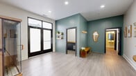 Located at 1000 Washington Ave in St. Louis, Missouri, this thoughtfully designed single-floor space offers a clean, modern aesthetic across two rooms and two bathrooms. The main open area greets visitors with light gray luxury vinyl plank flooring, recessed lighting, and striking sage-green accent walls that lend a calm, contemporary feel. Large black-framed glass double doors flood the space with natural light, creating an airy and welcoming atmosphere. A decorative wall-mounted mirror with an organic silhouette, floating shelves with greenery, and a wooden bench add warmth and personality to the entryway area. A hallway lined with dark-trimmed doors connects the main room to the secondary space, which features crisp white walls, recessed lighting, and a wooden console table flanked by framed botanical and abstract artwork — ideal for display or functional use. The two bathrooms are cleanly finished, with one showcasing subway tile detailing and a dark vanity, while the other offers a minimalist design with wood-toned flooring and simple, functional fixtures. Throughout the space, dark door frames and hardware provide a modern contrast against neutral walls, creating a cohesive and polished interior. The overall ambiance is calm, curated, and well-suited for a variety of uses.