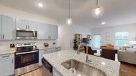 This well-appointed single-floor residence offers a cohesive and modern design aesthetic characterized by light-toned walls, warm wood-look flooring, and contemporary finishes throughout. The heart of the home is the open-concept kitchen, which features light gray shaker-style cabinetry with matte black hardware, granite countertops, a full suite of stainless steel appliances including a French door refrigerator, electric range, microwave, and dishwasher. A central island with an undermount sink and bar seating serves as a natural gathering point, illuminated overhead by stylish globe pendant lights with gold accents. The kitchen flows seamlessly into a dining area and a bright living room, where natural light pours in through multiple windows and a glass-paneled exterior door. The primary bedroom offers a ceiling fan, ample natural light, and a comfortable, airy atmosphere. The second bedroom provides a cozy retreat with a double-door closet. Both bathrooms continue the granite and gray cabinetry theme, each equipped with a shower-tub combination and wood-look flooring. The overall ambiance of this residence is clean, modern, and inviting, with thoughtful design details tying each space together seamlessly.