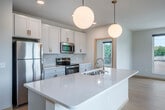 Located at 3920 Monona Dr in Madison, Wisconsin, this thoughtfully designed 2-bedroom, 2-bathroom residence offers a bright and contemporary living experience across a generous single-floor layout. Light wood flooring flows throughout, creating a warm and cohesive aesthetic.

The open-concept kitchen, dining, and living area serves as the heart of the home. The kitchen is outfitted with white shaker cabinetry accented by gold hardware, stainless steel appliances, a herringbone tile backsplash, and a large central island with a quartz countertop and undermount sink. Elegant globe pendant lights add a modern finishing touch.

The spacious primary bedroom benefits from a wall of large windows, filling the room with natural light and offering views of the surrounding neighborhood's lush greenery. It connects to a well-appointed en-suite bathroom featuring white cabinetry with warm-toned hardware, a broad vanity, and light wood flooring. A walk-in closet is accessible directly from the bathroom. The second bedroom also enjoys generous natural light through oversized windows with neighborhood views.

A conveniently located in-unit stacked washer and dryer is tucked behind light wood bi-fold doors in the hallway. The clean, neutral palette and modern design details throughout make this a bright, functional, and stylish home.