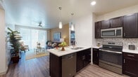 This single-story residence offers a thoughtfully designed open-concept layout that seamlessly connects the kitchen, dining, and living areas. The kitchen is a standout feature, equipped with dark espresso cabinetry, light quartz countertops, stainless steel appliances including a range, microwave, dishwasher, and refrigerator, along with a herringbone tile backsplash. A peninsula with bar seating and pendant lighting above serves as both a functional workspace and casual dining area. Wood-style flooring extends throughout the main living spaces, adding warmth and cohesion.

The living room is bright and welcoming, with a ceiling fan, warm accent walls, and a large sliding glass door that floods the space with natural light and provides access to an outdoor area. The bedrooms are carpeted for comfort, each featuring windows with blinds and ceiling fans. The primary bedroom includes access to an en-suite bathroom with a wide vanity, light countertops, dark cabinetry, wood-style flooring, and a tub-shower combination. A second bathroom mirrors similar finishes. A walk-in closet is also visible off the primary bath, adding practical storage to the overall well-balanced floor plan.