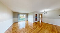 Located at 819 Marcy Ave in Oxon Hill, Maryland, this single-floor home offers a well-organized layout with a clean, move-in-ready aesthetic throughout. The main living and dining areas are anchored by gleaming hardwood floors that reflect natural light generously, creating a warm and inviting atmosphere. A large sliding glass door in the living area connects the interior to the outdoors, while a stylish geometric chandelier adds a contemporary touch to the dining space. Chair-rail molding runs along the walls, lending a classic architectural detail to the open layout. The kitchen is thoughtfully appointed with rich warm-toned wood cabinetry, dark granite countertops, a stainless steel sink, a gas range, and a striking mosaic tile backsplash in deep blue and black tones. Classic black-and-white patterned tile flooring completes the kitchen's distinct character. The bathroom features white subway tile surround, a tub-shower combination with a sliding glass enclosure, and a window that brings in natural light. The bedrooms are bright and spacious, each with hardwood flooring and windows overlooking greenery outside. Overall, the home presents a cohesive blend of classic and updated finishes throughout.