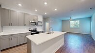 Located at 1501 Water Tower Circle in Greenville, SC, this well-appointed single-floor residence offers three bedrooms and three full bathrooms thoughtfully laid out for comfortable living. The open-concept kitchen and living area serves as the heart of the home, anchored by a large center island with a white quartz countertop and undermount sink. Gray shaker-style cabinetry, open shelving, and a full suite of stainless steel appliances — including a range, microwave, and refrigerator — complete the modern kitchen. Warm hardwood-style flooring runs throughout the main living areas, while a ceiling fan and natural light from a window create a bright, airy atmosphere in the living room. The three bedrooms feature plush carpeting, closets, and ceiling fans, with windows framing views of the surrounding greenery. The primary bedroom offers a generous footprint with its own dedicated bathroom. All three bathrooms are finished with light tile flooring, quartz vanity countertops, dark hardware accents, and glass-enclosed walk-in showers. Additional features include a dedicated laundry area and multiple closets for ample storage throughout the home.