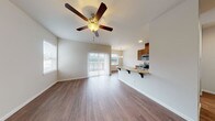 This well-appointed single-floor unit offers a thoughtfully designed open-concept layout that seamlessly connects the living area and kitchen. The living space features vaulted ceilings with a ceiling fan, warm hardwood-style flooring, and abundant natural light streaming in through multiple windows and a full sliding glass door that opens to an outdoor area. The open kitchen is equipped with rich wood cabinetry, granite-style countertops, stainless steel appliances including a range and refrigerator, and a breakfast bar with seating — ideal for casual dining. A pendant chandelier adds a decorative touch above the dining nook adjacent to the kitchen. The bedroom is a generously sized, quiet retreat with its own ceiling fan, hardwood-style flooring, and neutral wall tones. The unit includes two bathrooms: one featuring a wood-cabinet vanity with a granite-style countertop and a walk-in shower with a clean, all-white surround, and a second with a matching vanity, toilet, and hardwood-style flooring. Throughout the space, the consistent use of neutral tones, warm wood finishes, and hardwood-style flooring creates a cohesive and inviting ambiance.