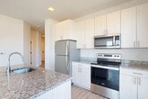 Located at 7730 Harkins Rd in Lanham, MD, this well-appointed 2-bedroom, 2-bathroom residence offers a thoughtfully designed single-floor layout. The open-concept kitchen and living area serves as the heart of the home, featuring light wood-style flooring, recessed lighting, and large windows that invite abundant natural light and outdoor views. The kitchen is equipped with stainless steel appliances — including a refrigerator, range, and over-the-range microwave — complemented by white cabinetry extending to the ceiling, granite countertops, and a central island with a sink, ideal for both cooking and entertaining. The living area connects seamlessly to one of two private balconies, extending the living space outdoors. Both bedrooms are carpeted and well-sized, with the primary bedroom offering generous proportions and ample closet space. The second bedroom features a large window with open views of the surrounding area. Each bathroom is finished with granite-topped vanities, illuminated mirrors, and wood-style flooring. Additional conveniences include in-unit laundry, four closets for storage, and a connecting hallway that ties the layout together efficiently. The clean, neutral palette throughout creates a bright and modern ambiance.