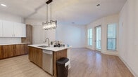 Located at 2124 American Industrial Way in Chamblee, GA, this thoughtfully designed one-bedroom, one-bathroom residence offers a modern open-concept layout with clean lines and contemporary finishes throughout. Light wood-style flooring flows across the main living areas, complementing the bright, neutral color palette that enhances the sense of openness.

The kitchen is a standout feature, showcasing two-tone cabinetry with white upper cabinets and warm wood-finish lower cabinets, a white quartz island with an undermount sink, stainless steel appliances including a French door refrigerator and microwave, a white subway tile backsplash, and a striking geometric pendant light fixture. The kitchen opens directly into the living area, which benefits from natural light and access to a private balcony through a glass-paneled door.

The spacious primary bedroom features plush carpeting, a large window with exterior views, and access to a walk-in closet outfitted with wire shelving and built-in storage cubbies. The bathroom is clean and functional, featuring floor-to-ceiling tile surrounding a soaking tub with an overhead shower, wood-look flooring, and chrome fixtures. A dedicated laundry area and hallway complete the efficient, well-organized floor plan.