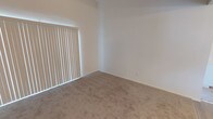 This single-floor residence offers a clean, functional layout with notable architectural details throughout. The bedrooms are generously proportioned, featuring soaring vaulted ceilings that amplify the sense of openness and volume. Plush wall-to-wall carpeting provides warmth underfoot, while large windows dressed with vertical blinds allow abundant natural light to fill the spaces and offer adjustable privacy.

The kitchen is designed in a practical U-shaped configuration, maximizing counter and storage space. White cabinetry lines the walls from floor to ceiling, complemented by white countertops and light wood-look flooring that lends a fresh, airy feel. The kitchen is equipped with a gas range, dishwasher, and a double-basin sink positioned beneath a window, offering natural light while cooking or cleaning. Overhead flush-mount lighting ensures the space remains well-lit throughout the day.

The bathroom features light wood-look flooring consistent with the kitchen, neutral walls, and a mirrored medicine cabinet above the vanity. A towel bar and shower with a decorative curtain complete the space, keeping it tidy and efficient. Throughout the residence, a neutral color palette of whites and warm beiges creates a cohesive, calm ambiance that is both inviting and easy to personalize.