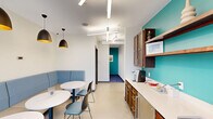 Located at 257 E Township St in Fayetteville, Arkansas, this single-floor amenity suite offers a thoughtfully designed collection of functional spaces suited for work, wellness, and social gathering. The layout encompasses a fitness center, two dining areas, a kitchenette, two private offices, and two conference rooms, all connected by well-defined hallways.

The fitness center is generously sized and outfitted with cardio machines, cable equipment, free weights, and benches, all set beneath geometric linear lighting. Full-length mirrors and a glass entry door with outdoor views contribute to an open, energizing atmosphere.

The dining areas feature comfortable blue upholstered booth seating, round white tables, and striking matte black pendant lights with gold interiors, creating a welcoming break space. Adjacent to the dining area, the kitchenette includes warm-toned wood cabinetry, white countertops, open shelving, and a bold teal accent wall that carries throughout the suite as a unifying design element.

The two private offices each provide a focused workstation with a desk, ergonomic chair, wall sconce lighting, and framed landscape artwork against the signature teal wall. The conference rooms offer round wood tables, cream upholstered chairs, geometric pendant lighting, and wall-mounted displays, ideal for collaborative meetings.