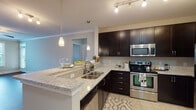 This single-story residence combines contemporary finishes with functional design throughout its thoughtfully arranged layout. The kitchen serves as a central highlight, showcasing rich dark espresso cabinetry that extends to the ceiling for ample storage, light-toned granite countertops, and a full suite of stainless steel appliances including a range, built-in microwave, dishwasher, and refrigerator. A peninsula with pendant lighting overhead provides additional counter space and casual dining potential, while tile flooring and track lighting complete the culinary space.

The living area features warm, dark hardwood flooring, crown molding, a ceiling fan, and large windows that invite generous natural light and outdoor views, creating an open and airy atmosphere. A secondary bedroom offers plush carpeting, a ceiling fan, and a window overlooking the exterior. The bathroom is finished with the same granite countertops and dark cabinetry found in the kitchen, paired with a tub-shower combination and tile flooring. A dedicated walk-in closet with wire shelving provides organized storage, while a separate in-unit laundry closet accommodates a full-size washer and dryer.