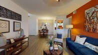 This well-appointed single-floor residence showcases a thoughtfully designed open-concept layout that connects the living, dining, and kitchen areas in a seamless flow. The living room is a standout space, anchored by a bold burnt-orange accent wall, rich hardwood-style flooring, and a corner fireplace that adds warmth and character. Natural light filters in through large windows dressed with patterned curtains, and a private exterior door provides convenient outdoor access directly from this room.

The dining area sits adjacent to the living space, centered around a glass-top round table beneath a pendant light fixture, with additional wall décor contributing to a welcoming atmosphere. The galley-style kitchen features white cabinetry, light countertops, full appliances, and a striking orange accent wall that ties together the communal areas.

The primary bedroom offers plush carpeting, a ceiling fan, a natural-light window, and ample closet space, while the second bedroom features its own bold orange accent walls and a well-sized closet. The bathroom is clean and functional, complete with a tub-shower combination, hardwood-style flooring, and a single vanity. Throughout the residence, consistent design choices — including hardwood-style floors, ceiling fans, and vibrant accent colors — create a cohesive and lively living environment.