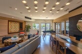 Located at 202 Mosley Ave in Alameda, CA, this single-floor community amenity space at Admirals Cove serves as a vibrant hub for recreation and social gathering. The open-plan layout is finished with warm light wood flooring throughout, creating a cohesive and inviting atmosphere.

The lounge area centers around a distinctive organic wood-base glass coffee table surrounded by woven accent chairs and deep blue cube ottomans, offering a relaxed and stylish setting. A standout feature is the oversized built-in Scrabble board mounted on a shiplap-paneled wall, accompanied by a chalkboard panel — a charming and unique focal point. Below it, a low-profile storage credenza provides additional functionality.

The dining area features a long communal table with ample seating, positioned against a dramatic dark-tiled fireplace wall with a round mirror centerpiece. Large sliding glass doors alongside tall windows flood the space with natural light and provide direct access to an outdoor area.

A foosball table adds a playful, recreational element near the dining zone. The kitchenette is equipped with marble-look quartz countertops, warm wood cabinetry, stainless steel appliances, and a picture window framing outdoor greenery. The ceiling throughout features an architectural grid of recessed spotlights, enhancing the modern, well-lit ambiance of the entire space.