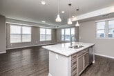 This single-floor unit offers a well-designed layout spanning a comfortable footprint, accommodating two bedrooms and two full bathrooms. The open-concept kitchen and living area serves as the heart of the space, where light wood-tone flooring extends throughout. The kitchen is appointed with taupe shaker-style cabinetry, a white subway tile backsplash, stainless steel appliances including a range, microwave, and refrigerator, and a central island topped with striking veined quartz countertops. Three pendant lights hang above the island, adding a modern touch. An in-unit stacked washer and dryer is conveniently located adjacent to the kitchen.

The living area is generously sized, bathed in natural light from multiple windows with horizontal blinds. Neutral-toned walls carry throughout the unit, creating a cohesive and calming atmosphere. Both bedrooms feature plush carpeting and windows providing natural light. The primary bedroom includes a spacious walk-in closet outfitted with wire shelving systems.

The primary bathroom features a dual-sink vanity with quartz countertops, wood-look flooring, and a separate shower. The second bathroom offers a full tub-shower combination with brushed nickel fixtures and a single vanity.