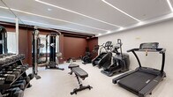 Located at 1151 E Main St in Meriden, Connecticut, this fitness center offers a well-appointed, single-floor workout space designed to support a full range of exercise routines. The interior features a clean, modern aesthetic defined by a light-toned floor, crisp white ceilings, and bold deep-red accent walls that create an energizing atmosphere. Sleek linear LED lighting runs across the ceiling, providing bright, even illumination throughout the space.

The facility is comprehensively equipped for both cardiovascular and strength training. Cardio equipment includes a treadmill, elliptical machine, stair climber, stationary bike, and a rowing machine, offering diverse options for aerobic workouts. On the strength side, the space features a multi-functional cable machine system, a full dumbbell rack with an extensive range of weights, adjustable benches, and a dedicated area for functional training accessories including resistance bands, medicine balls, and exercise mats.

A mirrored wall on one side visually expands the space while providing a practical training reference. A glass-paneled entry door adds a polished, professional feel to the entryway. The layout is thoughtfully organized to allow ample room to move between stations. Overall, this fitness center delivers a well-rounded, professional-grade workout environment in a compact yet highly functional footprint.