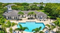 This 2-bedroom, 1-bathroom model townhome at St. Tropez Luxury Townhomes and Villas in Plantation spans 1,340 square feet across three floors. The ground floor (290 sq ft) features a dedicated laundry area with full-size washer hookups and staircase access. The main living level (710 sq ft) showcases an open-concept kitchen and living room with light wood-style flooring, vaulted ceilings with recessed track lighting, and a tray ceiling detail. The gourmet kitchen features white shaker cabinetry, stainless steel appliances, a mosaic tile backsplash, and a granite waterfall island with bar seating. The living area is bright and airy, with sliding glass door access and a ceiling fan. The upper floor (340 sq ft) hosts both bedrooms and the full bathroom. The primary bedroom (170 sq ft) features vaulted ceilings, plush carpeting, a ceiling fan, and a walk-in closet. The secondary bedroom offers similar comfort with carpeted floors. The shared bathroom includes a granite vanity, white cabinetry, wood-style flooring, and a tub-shower combination with white tile surround.