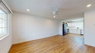 This well-appointed single-floor residence offers a clean, modern aesthetic defined by warm honey-toned hardwood-style flooring that extends seamlessly throughout the entire space. The open living area is generously proportioned, bathed in natural light from a front-facing window, and equipped with a ceiling fan and recessed lighting, creating a bright and comfortable atmosphere.

The kitchen is a functional highlight, featuring crisp white cabinetry with matte black hardware, stainless steel appliances including a range, microwave, and dishwasher, a stainless undermount sink, and light countertops. A skylight-style flush fixture provides additional illumination, making the kitchen feel open and airy.

The bedrooms are spacious and well-lit, each outfitted with ceiling fans. Notable is a primary bedroom with sliding glass doors that open directly to a private balcony, offering outdoor views and fresh air. A second bedroom also benefits from a large window with exterior views.

The bathroom is finished with neutral tile flooring and wall tile surround, and includes a full soaking tub with shower. The overall layout, as seen in the dollhouse view, is thoughtfully organized with clear separation between living, sleeping, and kitchen zones, delivering a cohesive and functional living environment.