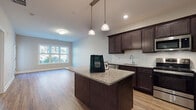 Located at 60 Beard in Shelton, Connecticut, this single-floor residence offers a thoughtfully designed layout with contemporary finishes throughout. The kitchen serves as a central highlight, showcasing rich dark-espresso cabinetry paired with granite countertop surfaces, a subway tile backsplash, and a full suite of stainless steel appliances including a refrigerator, range, microwave, and dishwasher. A central island with pendant lighting above provides additional prep space and casual seating potential, while a window at the far end of the adjoining dining area allows natural light to filter into the space.

Warm wood-look flooring runs continuously throughout the unit, creating a cohesive and inviting atmosphere. The open layout between the kitchen and living areas promotes a sense of spaciousness and ease of flow. Individual rooms are well-proportioned, with neutral gray wall tones that complement the overall modern aesthetic.

The bathroom is clean and functional, featuring a walk-in shower, a granite-topped vanity with white cabinetry, and consistent wood-look flooring. A hallway connecting the bathroom to the kitchen provides convenient access between the private and common areas of the unit.
