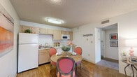 Located at 7401 Phoenix Ave in El Paso, TX, this single-floor, one-bedroom, two-bathroom residence offers a thoughtfully organized layout that makes efficient use of its space. The open-plan living area seamlessly combines the kitchen, dining, and living room into one cohesive zone. The kitchen features light wood cabinetry, white appliances including a refrigerator, electric range, microwave, and dishwasher, all set above durable hardwood-style flooring. A round dining table sits adjacent to the kitchen, creating a natural flow for everyday meals. The living room is carpeted and anchored by a large window that invites natural light and outdoor views, giving the space an airy, welcoming feel. A textured ceiling carries throughout the unit. A carpeted hallway connects the main living areas to the private bedroom, which is generously proportioned and features two windows with outdoor views, soft carpet underfoot, and a textured ceiling. Two closets provide practical storage. The two bathrooms include a full tub/shower combination. The unit's neutral color palette and warm accents create a calm, comfortable atmosphere throughout.