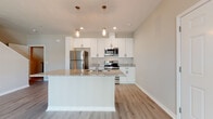 Located at 3301 Whitney Rd in Largo, Florida, this two-story home offers a clean, modern design with consistent finishes throughout. The main level centers on an open-concept layout where the kitchen flows seamlessly into the living area. The kitchen is outfitted with white shaker-style cabinetry, granite countertops, stainless steel appliances including a refrigerator, range, and microwave, and a central island with a built-in sink. Pendant lighting with an industrial-style mason jar aesthetic illuminates the island, while recessed lighting and a ceiling fan keep the living space bright and comfortable. Light wood-tone luxury vinyl plank flooring runs throughout the main level, lending a cohesive, contemporary feel. A staircase leads to the upper floor, where carpeted bedrooms provide a softer, quieter environment. Each bedroom benefits from natural light through window blinds. The bathrooms feature white shaker vanities topped with granite countertops, round mirrors, and matte black hardware accents, with a full tub-and-shower combo available in the upper-level bath. A dedicated laundry closet houses a full-size washer and dryer. The overall palette of warm neutrals and white trim creates a bright, move-in-ready atmosphere throughout.