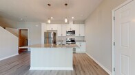 Located at 3301 Whitney Rd in Largo, Florida, this two-story home offers a clean, modern design with consistent finishes throughout. The main level centers on an open-concept layout where the kitchen flows seamlessly into the living area. The kitchen is outfitted with white shaker-style cabinetry, granite countertops, stainless steel appliances including a refrigerator, range, and microwave, and a central island with a built-in sink. Pendant lighting with an industrial-style mason jar aesthetic illuminates the island, while recessed lighting and a ceiling fan keep the living space bright and comfortable. Light wood-tone luxury vinyl plank flooring runs throughout the main level, lending a cohesive, contemporary feel. A staircase leads to the upper floor, where carpeted bedrooms provide a softer, quieter environment. Each bedroom benefits from natural light through window blinds. The bathrooms feature white shaker vanities topped with granite countertops, round mirrors, and matte black hardware accents, with a full tub-and-shower combo available in the upper-level bath. A dedicated laundry closet houses a full-size washer and dryer. The overall palette of warm neutrals and white trim creates a bright, move-in-ready atmosphere throughout.