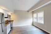 Located at 55 Bradford St in Providence, Rhode Island, this one-bedroom, one-bathroom residence offers a thoughtfully organized single-floor layout. The open-concept living, dining, and kitchen area serves as the heart of the home, featuring light hardwood-style flooring, vaulted ceilings with an exposed beam detail, and a set of windows that invite natural light and street views. The kitchen is equipped with white cabinetry, dark countertops, stainless steel appliances including a range and microwave, creating a functional and clean workspace directly accessible from the living area. A hallway connects the main living space to the private quarters, with a thermostat control panel and an electrical panel accessible along the corridor. The bedroom is a comfortable, well-proportioned room finished with neutral carpet, soft wall tones, and a set of double sliding closet doors offering generous storage. A second closet provides additional storage convenience. The full bathroom features slate-toned tile flooring, a glass-door walk-in shower, a white vanity, and built-in open shelving for organized storage. The overall aesthetic is clean, modern, and neutral, making this a versatile and move-in ready space in the heart of Providence.