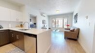 This well-designed 2-bedroom, 2-bathroom unit offers a thoughtful layout across a single floor. The open-concept kitchen and living area serves as the heart of the space, where a sleek kitchen features two-toned cabinetry — white uppers paired with dark lower cabinets — complemented by a white quartz peninsula with bar seating, a subway tile backsplash, and a full suite of stainless steel appliances. Light hardwood flooring runs throughout, lending a cohesive and bright feel to every room.

The living area is bathed in natural light from large windows that frame views of the surrounding urban landscape. A wall-mounted mini-split unit provides climate control in both the living area and the primary bedroom. The primary bedroom includes a built-in closet and direct hallway access to the in-unit laundry.

Both bathrooms are finished with clean white tile surround tub-shower combinations, light wood-look flooring, and dark wood vanities with light countertops. The second bedroom is a comfortable, well-proportioned room with its own window. A hallway connects all rooms efficiently, and a dedicated closet adds additional storage. The overall aesthetic is contemporary and clean, ideal for modern living.