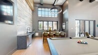 Located at 155 S 600 W in Salt Lake City, Utah, this single-floor community space is a masterfully designed open-concept living area that seamlessly blends modern aesthetics with functional versatility. Dramatic double-height ceilings with exposed dark wood beams create an expansive, loft-like atmosphere, while large black-framed windows and floor-to-ceiling glass walls flood the interior with abundant natural light and offer views of the surrounding urban neighborhood.

The living room serves as the heart of the space, featuring distinct zones for socializing and recreation. A plush seating area with velvet lounge chairs and a textured area rug anchors one section, while a dedicated media lounge showcases a striking herringbone-patterned tile feature wall with a large mounted display. A billiards table adds a recreational focal point to the open floor plan.

A wet bar and prep area with dark stone countertops, a sink, and a beverage station complement a stylish granite kitchen island with bar seating. A long counter-height bar runs along a wall of windows, providing additional seating with an abundance of natural light. Warm wood-look tile flooring flows throughout, tying together the layered stone accent walls and natural wood ceiling details. Multi-panel glass doors open directly to an outdoor patio, enhancing the indoor-outdoor connectivity of this thoughtfully curated space.