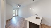 Located at 207 Gresham Ln in Mooresville, NC, this single-floor residence showcases a modern design with clean lines, warm wood-look flooring, and a bright, neutral color palette throughout. The open-concept living and dining area flows seamlessly toward glass French doors that invite natural light and provide access to an outdoor space, while a ceiling fan overhead adds comfort and character.

The kitchen is a standout feature, equipped with dark, sleek cabinetry paired with white quartz countertops and a geometric-patterned tile backsplash. Stainless steel appliances — including a range, over-the-range microwave, and refrigerator — complete the space. A built-in wine rack adds a distinctive touch, and pendant lighting over the kitchen island creates an inviting atmosphere for entertaining.

The bedrooms are well-appointed with wood-look flooring, ceiling fans, and generous natural light from large windows. A spacious walk-in closet with wire shelving provides ample storage. The bathroom is finished with full white subway tile surrounding the tub and shower, complemented by matte black fixtures, a dark-framed vanity mirror, and a wood-toned vanity cabinet. Every detail reflects a cohesive, contemporary aesthetic designed for comfortable, stylish living.