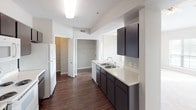 This single-floor residence offers a thoughtfully designed layout across two bedrooms and two bathrooms. The living area is a standout space, featuring soaring vaulted ceilings, a ceiling fan, and generous natural light streaming through a large picture window and glass French doors, creating an airy, open atmosphere. Light-toned carpeting and neutral wall colors contribute to a clean, cohesive aesthetic throughout.

The kitchen is equipped with dark espresso cabinetry, light countertops, a double sink, and white appliances including a refrigerator, electric range, and built-in microwave. A curved pass-through counter connects the kitchen to the main living area, enhancing the open-concept flow. An arched doorway adds a distinctive architectural detail, leading toward the bedroom corridor.

Both bedrooms feature plush carpeting, ceiling fans, and windows that bring in natural light and outdoor views. Each room offers comfortable proportions suitable for standard furnishings.

The two bathrooms are finished with dark cabinetry and light countertops. The primary bathroom includes an extended vanity with a large mirror and dark wall-mounted storage cabinets, while the secondary bathroom features a tiled tub-shower combination. Wood-look flooring runs through the kitchen and bathrooms, providing a practical contrast to the carpeted living and sleeping areas.