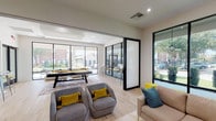 Located at 9111 Lakes at 610 Dr in Houston, Texas, this single-floor community amenity space is designed with a modern, energetic aesthetic that blends functionality with style. The open-plan layout is anchored by light hardwood flooring and crisp white walls, creating a bright and welcoming atmosphere throughout.

The game and lounge area serves as the centerpiece of the space, featuring a bold yellow pool table paired with comfortable, curved gray lounge chairs accented with vibrant yellow throw pillows. A cozy seating nook nearby offers a sofa with colorful cushions and a dark wood credenza topped with a striking yellow sculptural vase, accompanied by a wall-mounted display screen. Bold pop-art prints in black frames add a playful, gallery-like character to the walls.

Floor-to-ceiling black-framed glass windows and sliding doors wrap generously around the space, flooding the interior with natural light and offering views of the lush, tree-lined surroundings. A glass-partitioned section provides a semi-private area with high-top seating, ideal for casual meetings or social gatherings. Recessed ceiling lighting complements the abundant daylight, ensuring the space remains well-lit at all hours. The overall ambiance is lively, contemporary, and thoughtfully curated for community engagement.