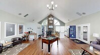 Located at 401 NC-54 W in Carrboro, NC, this single-floor community clubhouse offers an open-concept layout that seamlessly connects the living, dining, and kitchen areas into one cohesive and welcoming environment. The space is defined by dramatic vaulted ceilings that soar to impressive heights, amplifying the sense of openness throughout. A striking stacked-stone accent wall anchors the main gathering area, complemented by a wall-mounted television and an elegant chandelier that adds a refined touch.

Warm hardwood-style flooring runs throughout, tying the space together with a consistent, inviting aesthetic. Natural light pours in abundantly through large windows and a signature arched transom window, as well as through glass-paned French doors that open onto an outdoor deck with views of the surrounding area. The soft sage-green wall palette enhances the bright, airy atmosphere.

The kitchen features white cabinetry, stainless steel appliances, and a dark-countertop bar with seating for multiple guests. The living area accommodates comfortable lounge seating alongside recreational amenities including a foosball table. A separate seating nook with office-style windowed partitions provides a quieter setting. The space is well-suited for community gatherings, social events, and everyday relaxation.