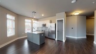 Located at 115 E 5th Ave in Columbus, Ohio's vibrant Short North area, this single-floor unit offers a thoughtfully designed open-concept layout with modern finishes throughout. The kitchen serves as the centerpiece, featuring a large granite-topped island with an undermount sink, two-tone cabinetry with white upper and gray lower cabinets, a geometric tile backsplash, stainless steel appliances including a French door refrigerator and range, and warm Edison-bulb pendant lighting. The expansive living area flows seamlessly from the kitchen, boasting rich dark hardwood flooring, a ceiling fan, and a generous bank of windows that flood the space with natural light and offer views of the surrounding neighborhood. The bedrooms are carpeted and well-lit, with multiple windows dressed in blinds, providing ample natural light. The primary bedroom includes a spacious walk-in closet with built-in shelving and rail systems. Both bathrooms are finished with granite-topped gray vanities, tile flooring, and glass-enclosed walk-in showers adorned with marble-look tile surrounds. The unit's consistent gray-toned palette, clean lines, and quality materials create a cohesive, contemporary aesthetic throughout.