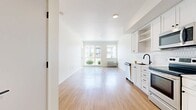 This 530-square-foot, one-bedroom, one-bathroom apartment at 7900 SE Luther Road in Portland, OR offers a clean, modern aesthetic throughout its single-floor layout. Light hardwood-style flooring runs continuously across all rooms, creating a cohesive and bright interior. The open-concept kitchen and living area serves as the heart of the unit, featuring white shaker-style cabinetry, a textured subway tile backsplash, stainless steel appliances including a refrigerator, electric range, microwave, and dishwasher, and a matte black faucet at the sink. The living area is filled with natural light from large sliding glass doors and windows that provide views of the surrounding grounds. A wall-mounted HVAC unit ensures year-round comfort. The 120-square-foot bedroom includes a dedicated closet with a built-in shelf and rod for organized storage. The bathroom features a full soaking tub and shower combination with white surround, complemented by a navy vanity with a light countertop and wood-style flooring. A separate closet provides additional storage within the unit. The overall ambiance is bright, clean, and move-in ready.