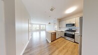 Located at 5 Lakeshore Center in Bridgewater, MA, this well-appointed two-bedroom, one-bathroom residence offers a thoughtfully designed single-level layout with modern finishes throughout. The open-concept kitchen and living area serves as the heart of the home, featuring warm hardwood-style flooring, crisp white shaker cabinetry, quartz countertops, a light blue tile backsplash, and a full suite of stainless steel appliances including a gas range, microwave, dishwasher, and refrigerator. Stylish pendant lighting hangs over the kitchen peninsula, which also houses a sink, creating a functional and inviting hub. The living room extends naturally from the kitchen, bathed in natural light from large windows that frame lush, wooded outdoor views. The primary bedroom is a comfortable retreat with its own access to a well-organized walk-in closet outfitted with built-in shelving and hanging rods. The second bedroom also enjoys generous natural light and scenic views through its large window. The full bathroom is finished with large-format neutral stone-look tile on both the floor and tub surround, complemented by gray cabinetry and a granite-topped vanity. Neutral tones and clean architectural lines create a bright, cohesive ambiance throughout the entire residence.