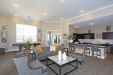 This single-floor communal space is thoughtfully designed to offer both comfort and functionality. The main lounge area serves as a welcoming focal point, featuring elegant double entry doors with arched transom windows that allow natural light to filter in. Crown molding, recessed lighting, and neutral-toned walls contribute to a polished, refined atmosphere throughout. Plush carpeting anchors the seating areas, which are furnished with upholstered sofas, wingback chairs, and sleek accent tables arranged to encourage both socializing and relaxation. A wall-mounted television and a fireplace with a textured accent wall provide a cozy entertainment corner.

A secondary seating nook, enclosed by large windows with plantation-style blinds, offers a quieter retreat with additional lounge chairs and a game table. The kitchen is well-equipped and stylishly appointed, featuring rich dark cabinetry, granite countertops, herringbone tile backsplash, light wood-look tile flooring, and stainless steel appliances including a range, microwave, refrigerator, and dishwasher. Ample counter space and storage make this kitchen highly functional. Together, the spaces create an inviting, upscale environment well-suited for community gatherings and everyday use.