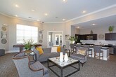 This single-floor communal space is thoughtfully designed to offer both comfort and functionality. The main lounge area serves as a welcoming focal point, featuring elegant double entry doors with arched transom windows that allow natural light to filter in. Crown molding, recessed lighting, and neutral-toned walls contribute to a polished, refined atmosphere throughout. Plush carpeting anchors the seating areas, which are furnished with upholstered sofas, wingback chairs, and sleek accent tables arranged to encourage both socializing and relaxation. A wall-mounted television and a fireplace with a textured accent wall provide a cozy entertainment corner.

A secondary seating nook, enclosed by large windows with plantation-style blinds, offers a quieter retreat with additional lounge chairs and a game table. The kitchen is well-equipped and stylishly appointed, featuring rich dark cabinetry, granite countertops, herringbone tile backsplash, light wood-look tile flooring, and stainless steel appliances including a range, microwave, refrigerator, and dishwasher. Ample counter space and storage make this kitchen highly functional. Together, the spaces create an inviting, upscale environment well-suited for community gatherings and everyday use.