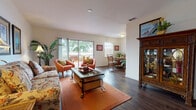 This well-appointed single-floor residence offers a harmonious blend of comfort and functionality across its thoughtfully designed layout. Rich, dark hardwood flooring runs throughout the main living areas, creating a warm and cohesive foundation for the space.

The spacious living room serves as the heart of the home, featuring clean white walls, ample natural light, and direct access to a private balcony through large sliding glass doors. The outdoor views of surrounding greenery lend the space a relaxed, nature-connected ambiance.

Flowing seamlessly from the living room, the dining area is bright and intimate, framed by a window overlooking the outdoors. It provides a charming setting for everyday meals and casual gatherings.

The galley-style kitchen is efficiently arranged with warm honey-toned wood cabinetry lining both sides, white appliances including a refrigerator, range, and dishwasher, and generous counter space. A passageway connects the kitchen directly to the rest of the home.

The bedroom is a restful retreat, featuring plush carpeting, soft ambient lighting, and a closet, offering a calm and comfortable environment.

The bathroom includes a dedicated vanity area with a large mirror and white cabinetry, separated from the shower and toilet area, providing both style and practicality. The overall ambiance of the home is warm, tropical-inspired, and welcoming.