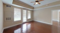 This single-floor space is defined by its polished concrete floors, which run consistently throughout the unit, providing a sleek, low-maintenance foundation that ties every room together. The warm beige walls and white trim create a neutral backdrop, complemented by ceiling fans in the main living and bedroom areas.

The kitchen is well-appointed with light maple cabinetry, dark granite countertops, and white appliances including a coil-burner range with over-the-range microwave and a full-sized refrigerator. Ample upper and lower cabinet storage is provided, along with a tall pantry-style cabinet for additional organization. Crown molding accents the kitchen's upper perimeter, adding a refined touch.

The open floor plan connects the living and dining areas fluidly, as seen in the overhead layout view. The main living area features a tray ceiling with crown molding detail and French-style doors offering natural light and outdoor views.

The bedrooms are generously sized, each receiving natural light through windows with exterior views and equipped with ceiling fans. One room features a built-in beam detail overhead.

The bathrooms maintain consistent finishes, featuring light maple vanities topped with dark granite countertops, wide mirrors with bar lighting, and a tub-shower combination with white tile surround. A louvered closet door adds a classic detail to the hallway.