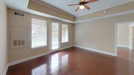 This single-floor space is defined by its polished concrete floors, which run consistently throughout the unit, providing a sleek, low-maintenance foundation that ties every room together. The warm beige walls and white trim create a neutral backdrop, complemented by ceiling fans in the main living and bedroom areas.

The kitchen is well-appointed with light maple cabinetry, dark granite countertops, and white appliances including a coil-burner range with over-the-range microwave and a full-sized refrigerator. Ample upper and lower cabinet storage is provided, along with a tall pantry-style cabinet for additional organization. Crown molding accents the kitchen's upper perimeter, adding a refined touch.

The open floor plan connects the living and dining areas fluidly, as seen in the overhead layout view. The main living area features a tray ceiling with crown molding detail and French-style doors offering natural light and outdoor views.

The bedrooms are generously sized, each receiving natural light through windows with exterior views and equipped with ceiling fans. One room features a built-in beam detail overhead.

The bathrooms maintain consistent finishes, featuring light maple vanities topped with dark granite countertops, wide mirrors with bar lighting, and a tub-shower combination with white tile surround. A louvered closet door adds a classic detail to the hallway.