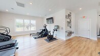 Located at 2076 Legacy Park Trail in Burlington, NC, this dedicated fitness center offers a spacious, single-floor layout designed to support a comprehensive workout experience. The room features warm hardwood-style flooring throughout, crisp white walls, and recessed lighting that creates a bright and energizing atmosphere. Multiple windows allow generous natural light to fill the space, enhancing the open and airy feel of the interior.

The cardio zone is well-appointed with multiple Spirit treadmills, a rowing machine, and a stationary cycle, all positioned to take advantage of the natural light. A wall-mounted flat-screen television accompanies this area, along with a motivational wall decal that reads, "If it doesn't challenge you, it doesn't change you." A water fountain is conveniently located nearby for hydration.

The strength training section includes an Axis cable machine system, a multi-function cable station, a dumbbell rack with a full range of weights, stability balls, and an adjustable workout bench. A wall-mounted mirror reflects light and allows users to monitor their form. The space also features a smart fitness mirror for guided workouts.

The facility is completed with a dedicated exit, recessed ceiling vents for climate control, and a clean, uncluttered layout that allows for comfortable movement between stations, making it a fully functional community fitness destination.